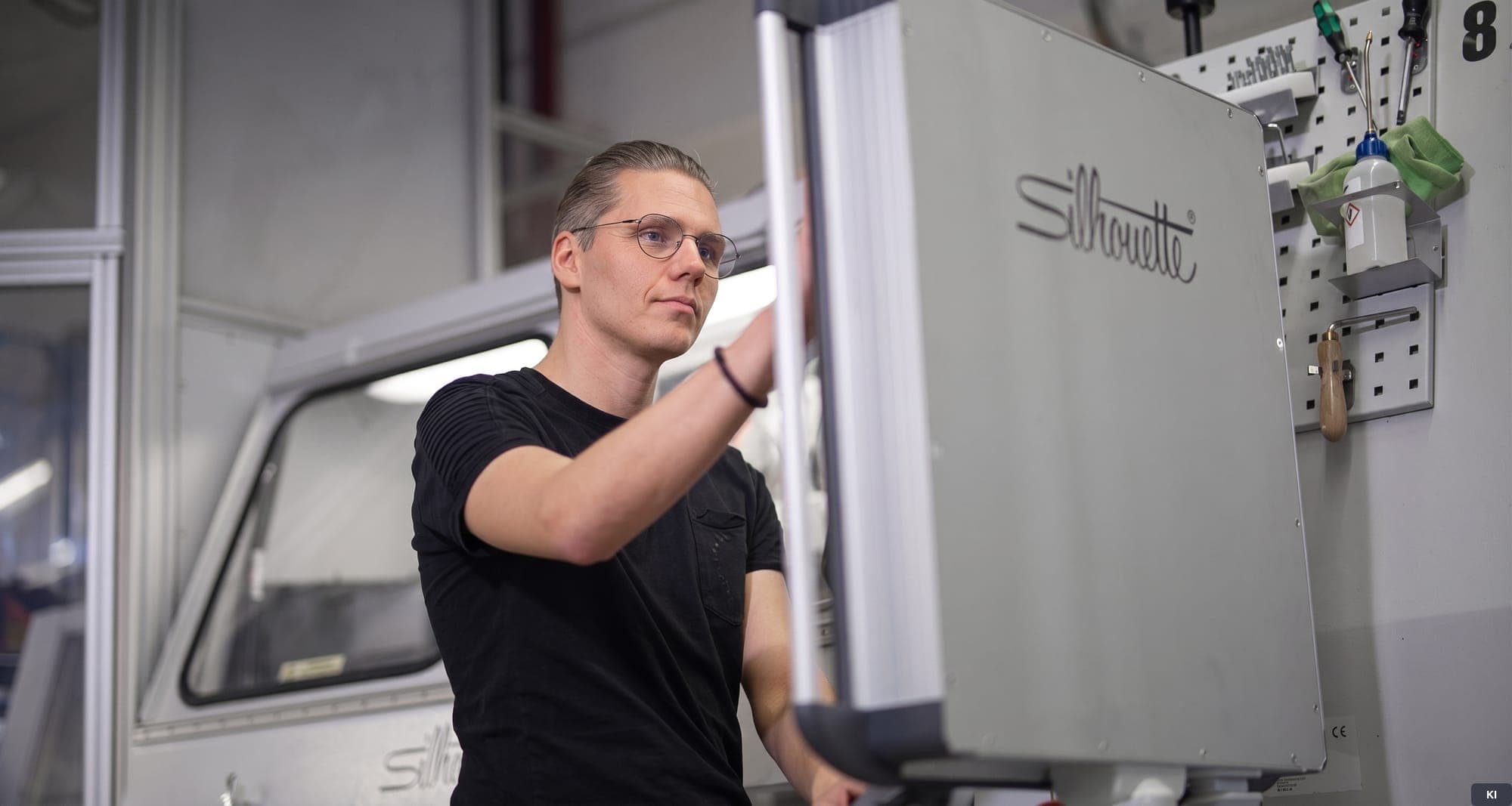 Techniker arbeitet an einer Fertigungsmaschine mit Silhouette-Schriftzug (KI-bearbeitetes Symbolbild)