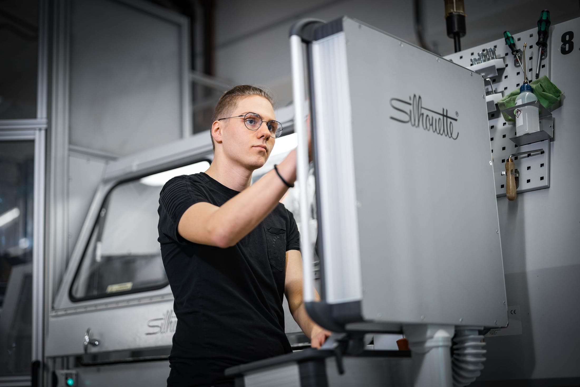 Techniker arbeitet an einer Fertigungsmaschine mit Silhouette-Schriftzug